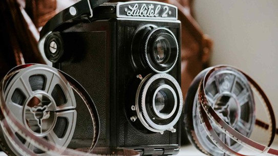 Vintage filmcamera met een grote lens en filmspoelen.