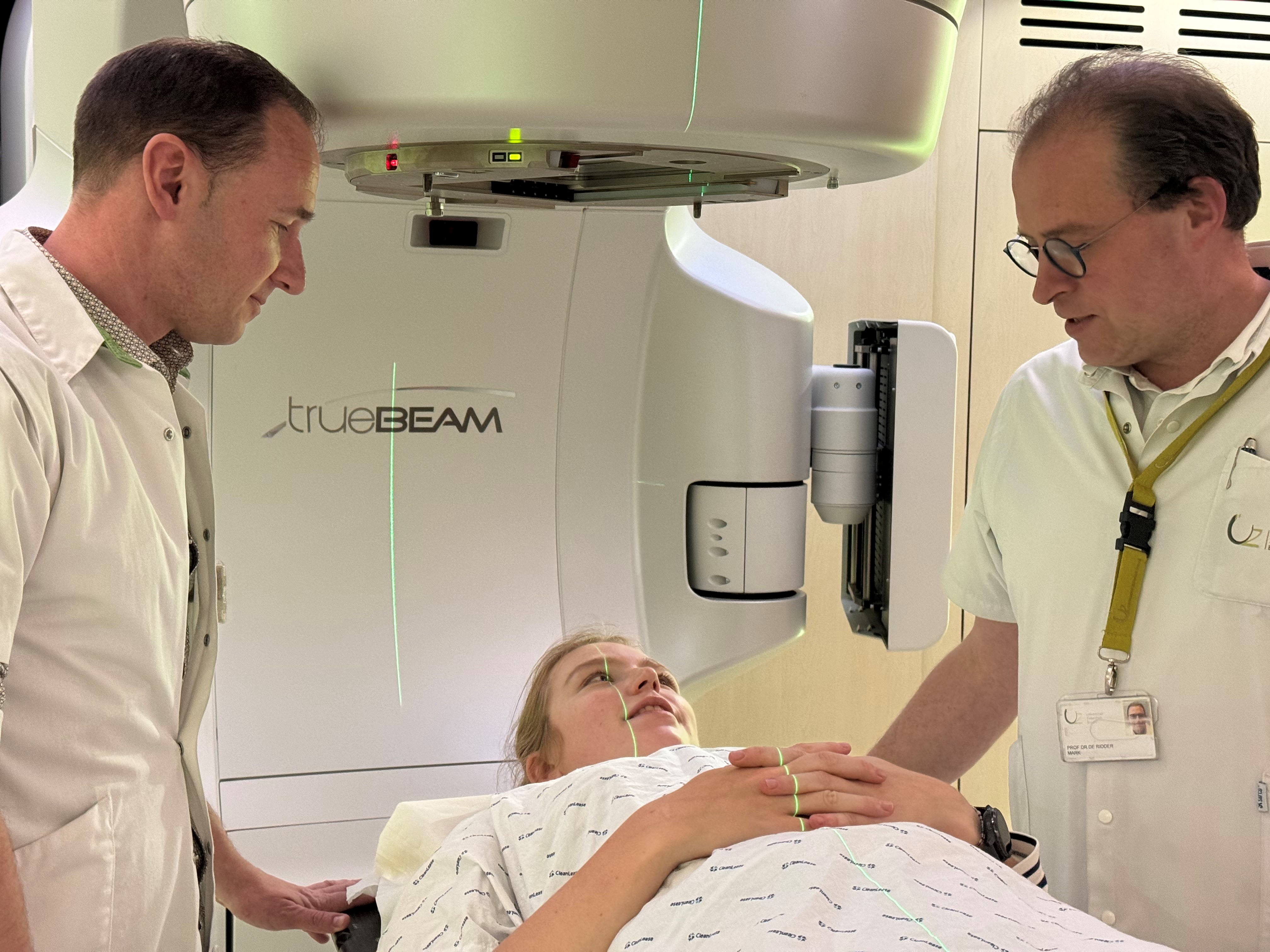 Twee personen in witte kleding staan naast een TrueBeam-medische machine in een klinische omgeving.