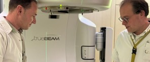 Twee personen in witte kleding staan naast een TrueBeam-medische machine in een klinische omgeving.