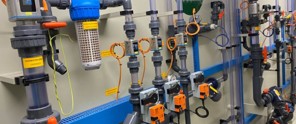 Close-up van een systeem van gekleurde buizen en ventielen met labels, gemonteerd op een muur voor technische instructies.