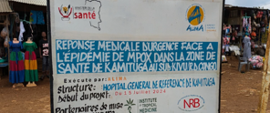 Bord met informatie over de medische respons op de mpox-epidemie in de gezondheidszone van Kamituga, inclusief contactgegevens voor hulpdiensten.