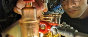 Wetenschapper in een laboratorium bestudeert vloeistoffen in glazen buizen onder een zwakke lichtbron.