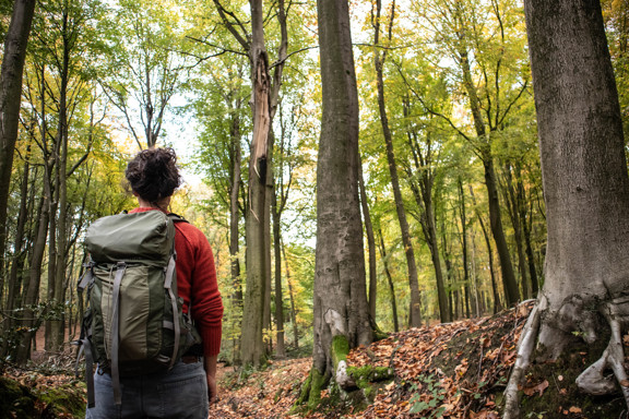 Een vrouw staat met haar rug naar de camera in een bos.