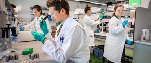 Wetenschappers in witte labjassen voeren experimenten uit in een laboratorium met pipetten en glazen bekers.