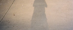 Schaduw van een persoon op een betonnen vloer, verlicht door licht vanuit de achtergrond.
