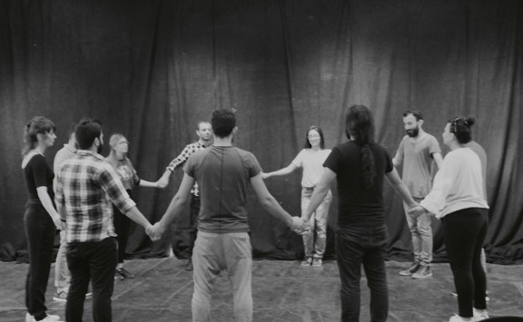 Een groep mensen staat in een cirkel en geeft elkaar de hand.