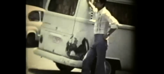 Beeld uit een film van een man die bij een volkswagenbusje staat