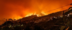 Een heuvel met huizen verlicht door een grote bosbrand, omgeven door een feloranje lucht.