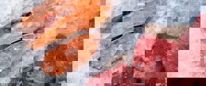 Freshly sliced salmon and pieces of red meat resting on a bed of ice.